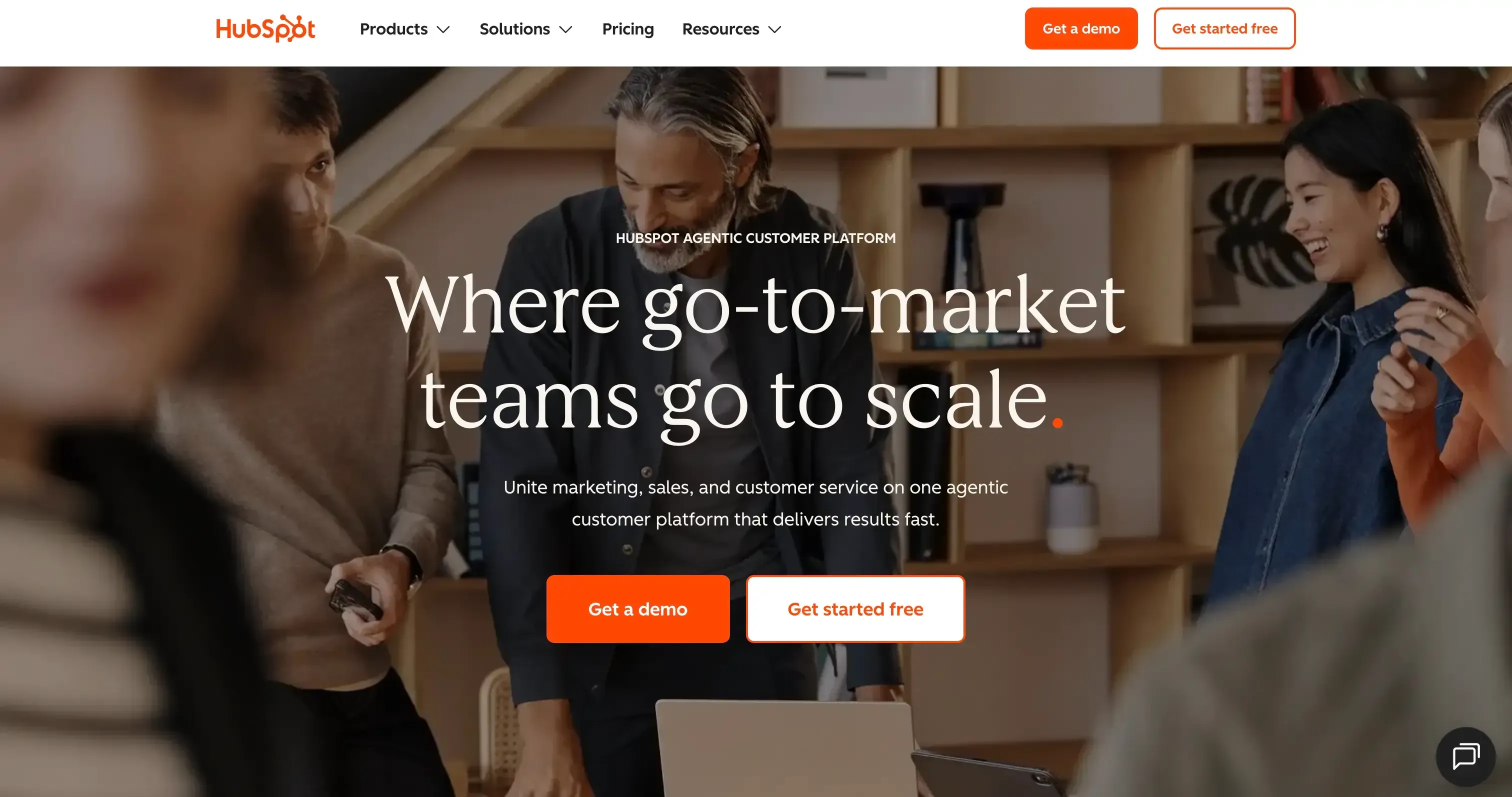 HubSpot homepage showing a team collaborating around a laptop with marketing and sales messaging.